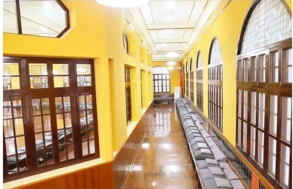 Corredor de paredes amarelas com janelas de madeira e uma fileira de almofadas encostadas na parede