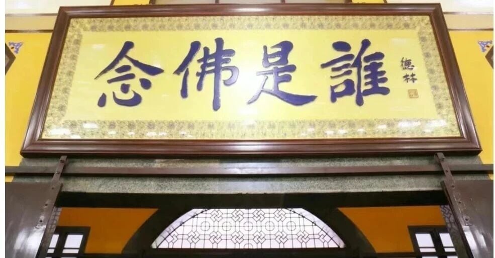 Placa de madeira com a inscrição 念佛是誰 em caligrafia sobre fundo amarelo
