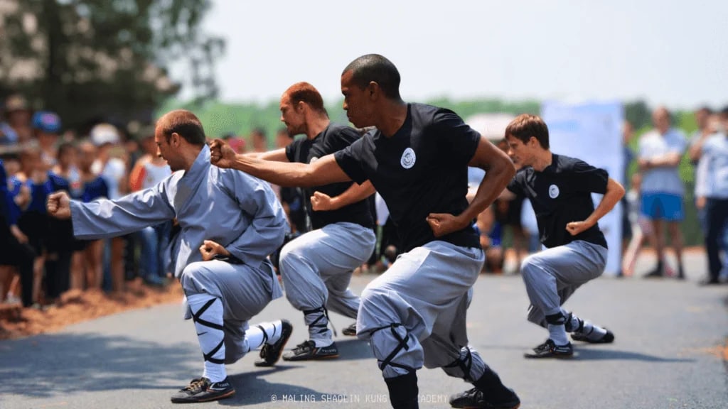 Alunos estrangeiros em demonstração de kung fu ao ar livre, com público ao fundo