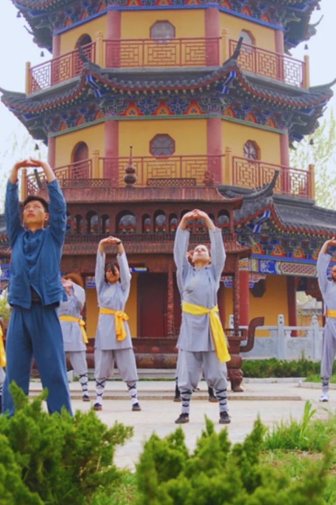 Alunos praticando qigong com as mãos erguidas diante de uma pagoda colorida
